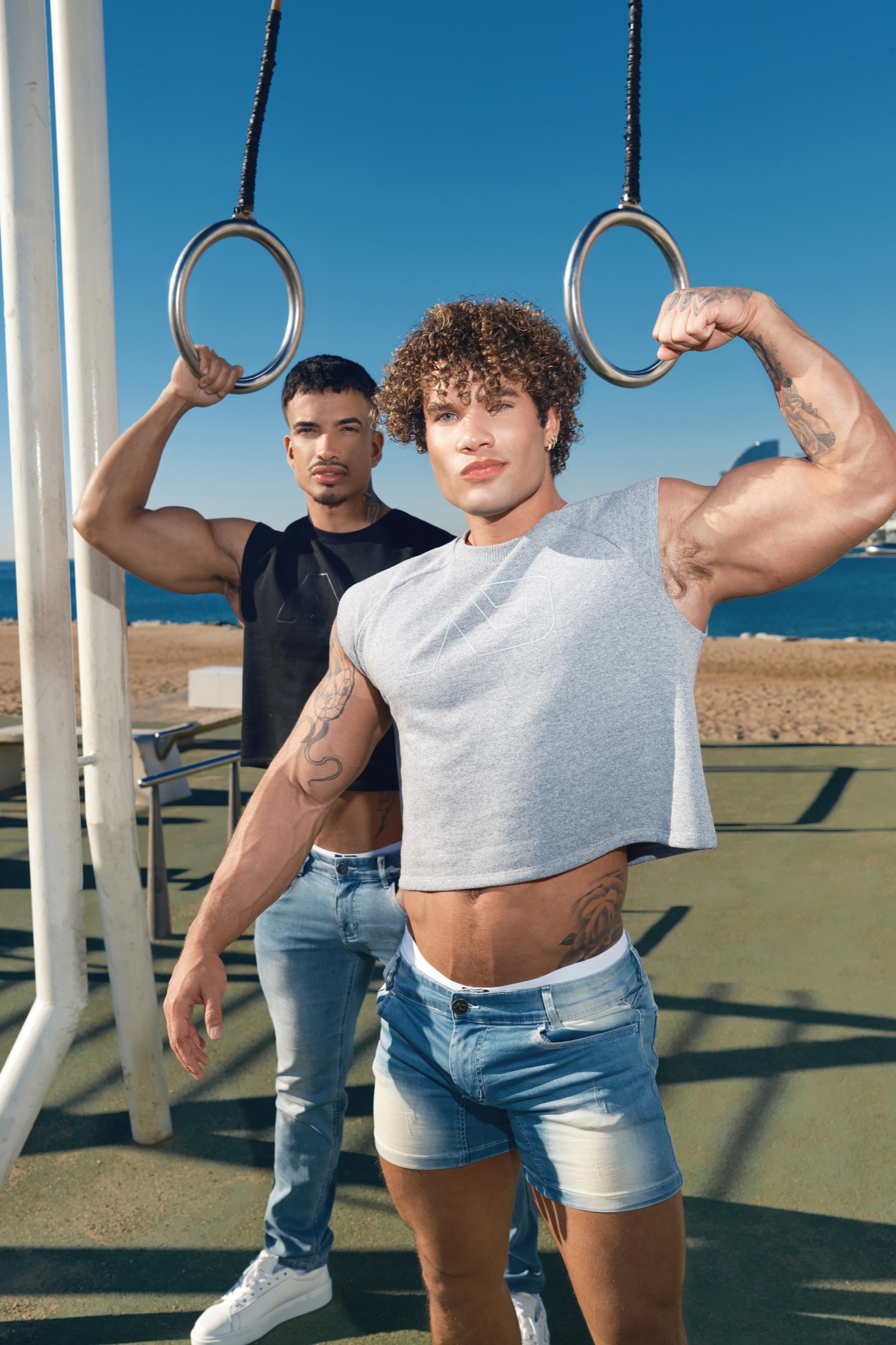 Two ADDICTED models in sleeveless tops and denim beside outdoor gym rings