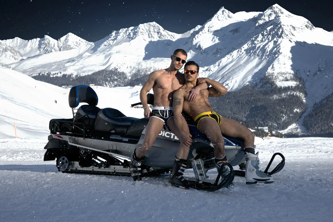 Two ADDICTED models in swim briefs seated together on a snowmobile