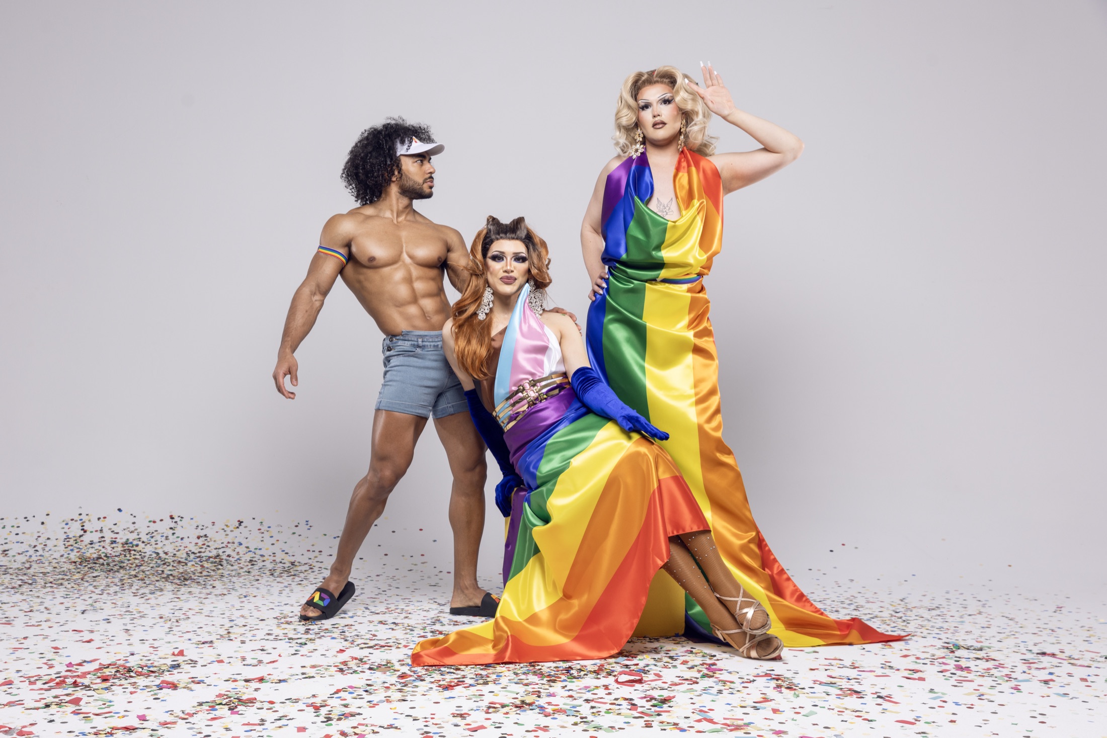 A model and two drag performers in rainbow-coloured outfits