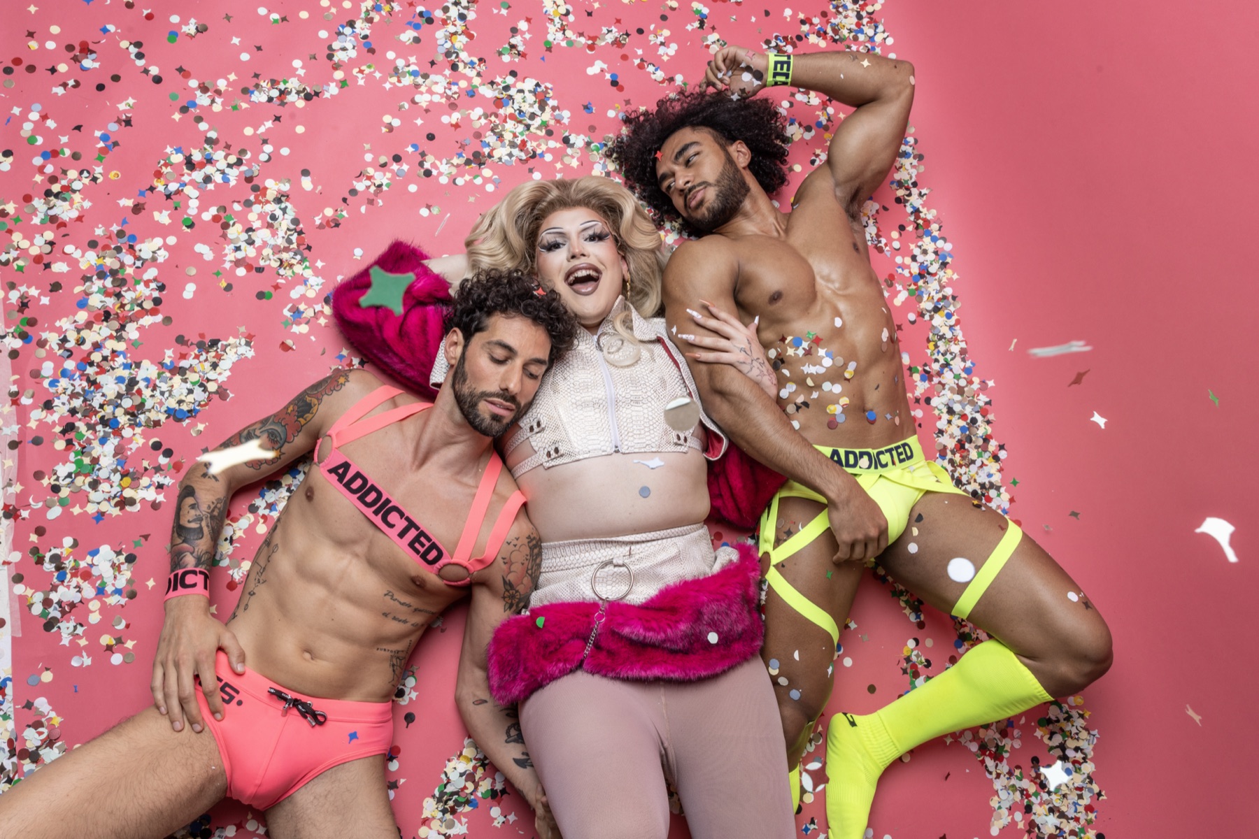 Drag előadó két ADDICTED-modellel rózsaszín háttér előtt