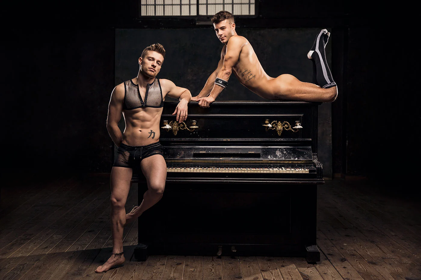 Two models in black party looks posed beside a piano