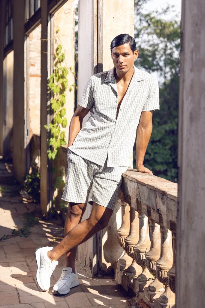 ES Collection model in an open white shirt and grey shorts on a shaded terrace