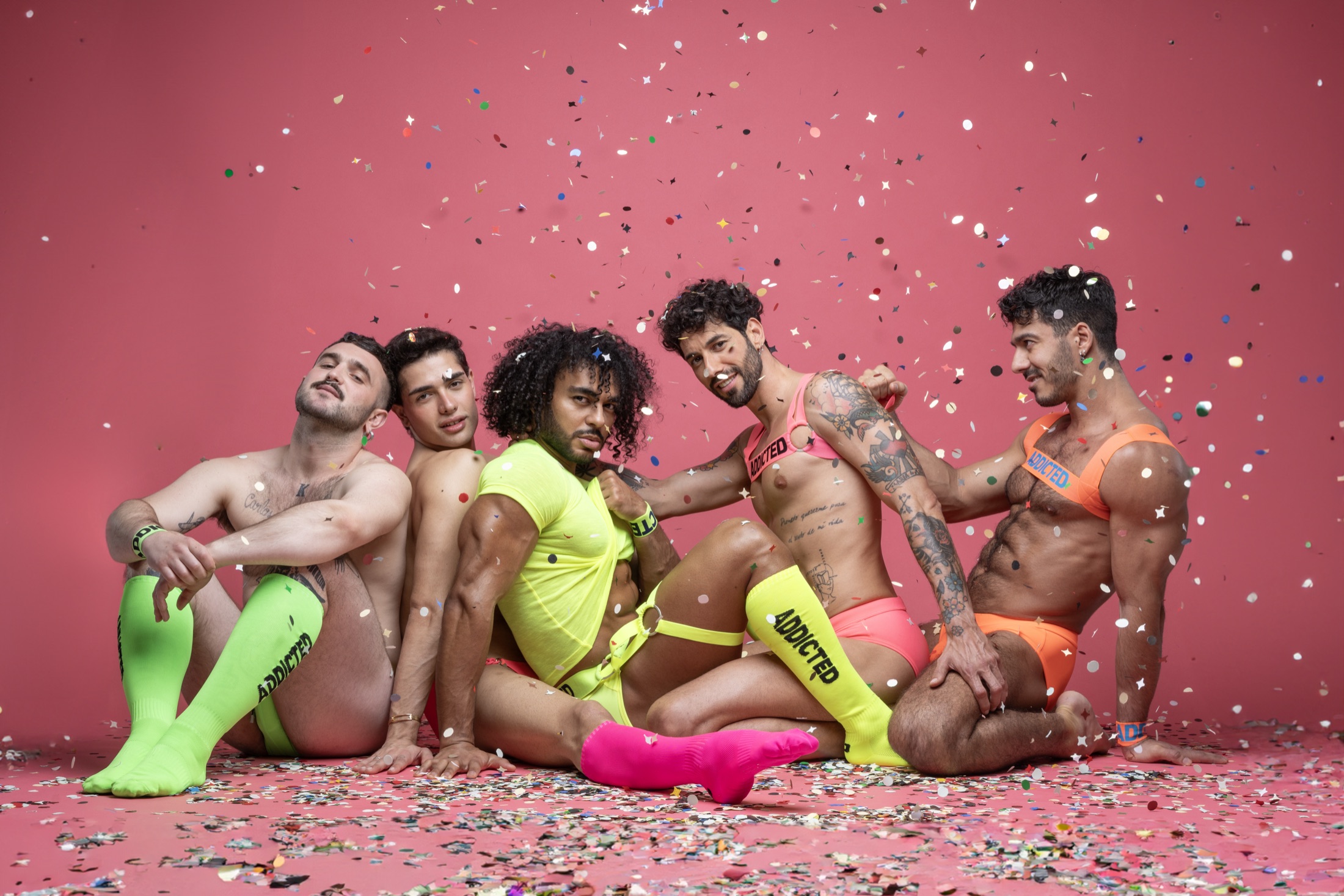 Five models in neon ADDICTED Pride outfits surrounded by confetti